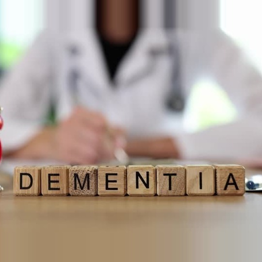Doctor writing at a desk beside wooden blocks spelling DEMENTIA