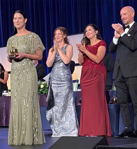 Elizabeth O'Connor holding a Golden Apple award on stage as three people applaud