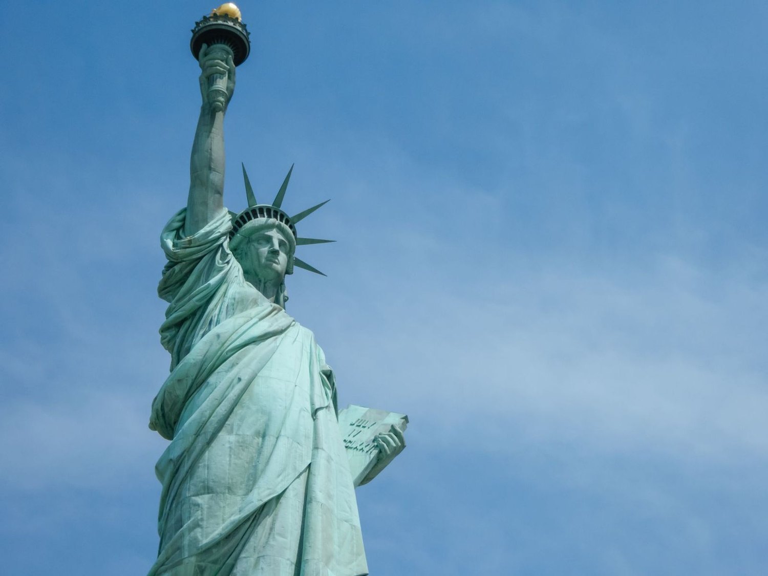 Statue of Liberty raising her torch against a blue sky