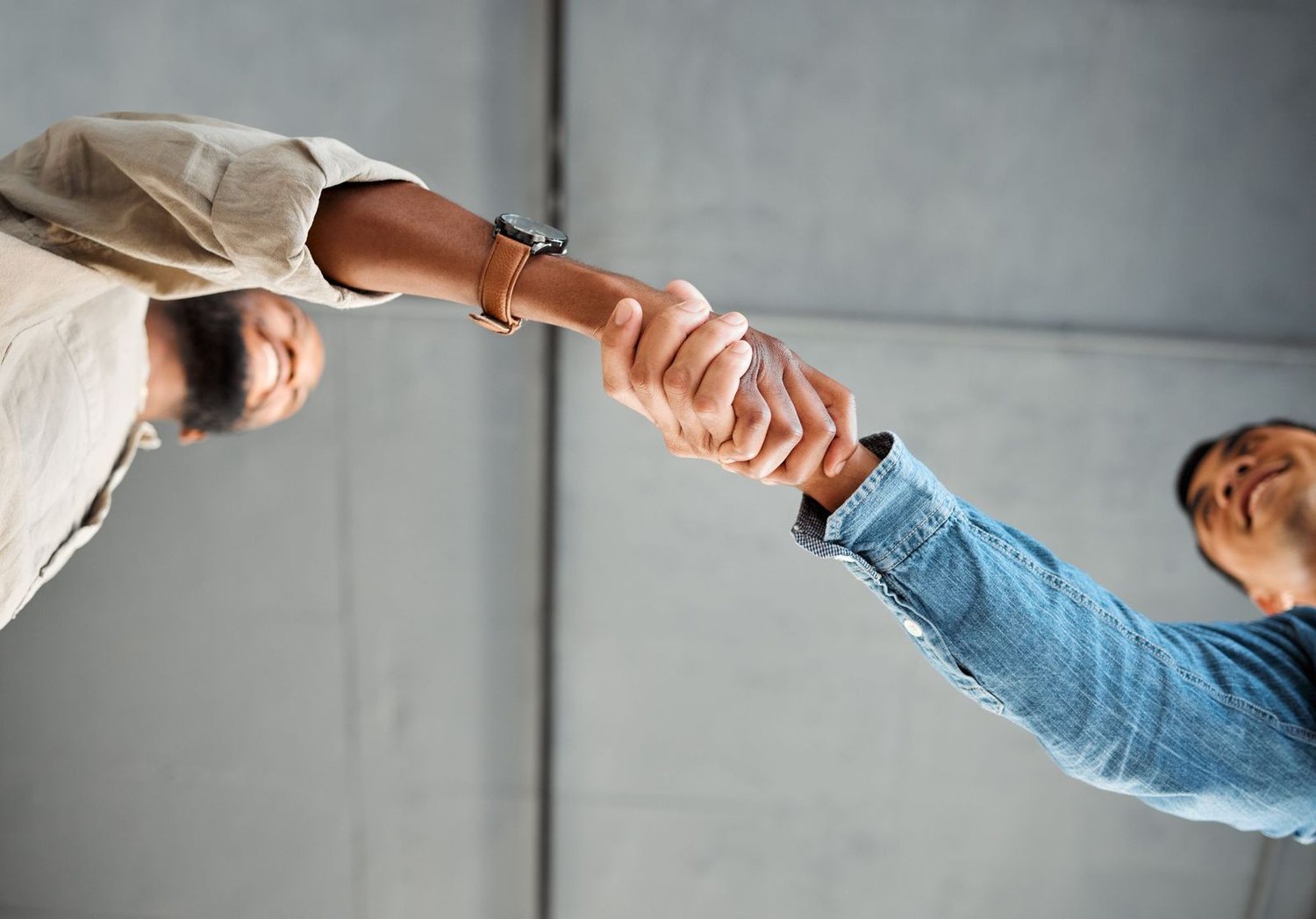 Two people shaking hands against a concrete wall